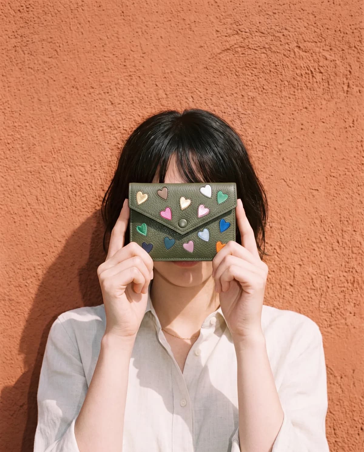 Bisou forest-green leather clutch with colourful hearts, held in hand — Suki Paris